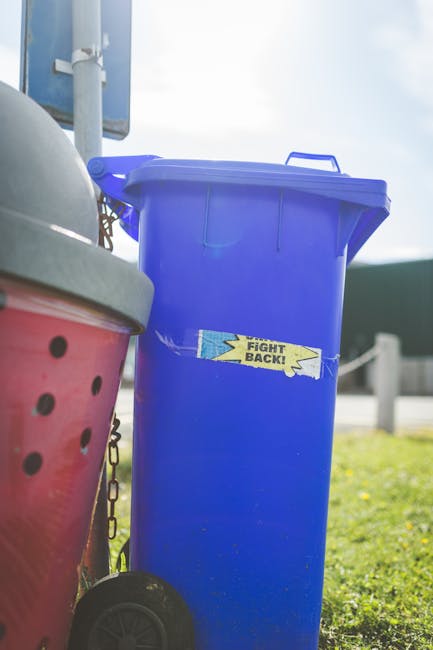 The image depicts a collection of clutter and waste materials situated on a paved driveway, which appears to be part of a residential or commercial property. In the foreground, there are various items
